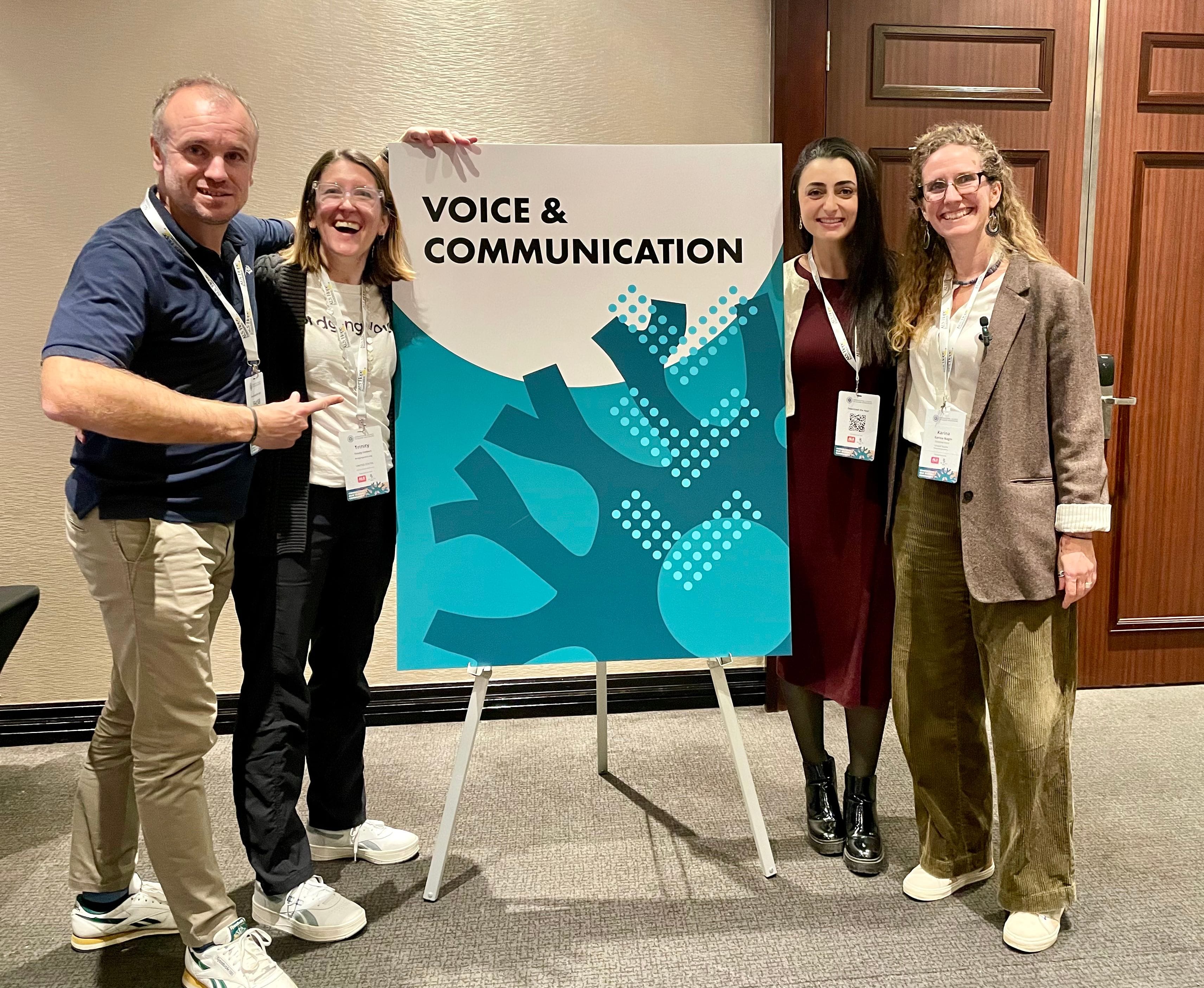 4 people smiling and standing around a sign that says "Voice & Communication"