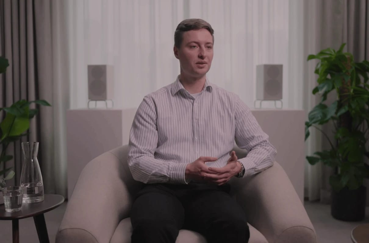 Man seated in an armchair speaking in a softly lit room.