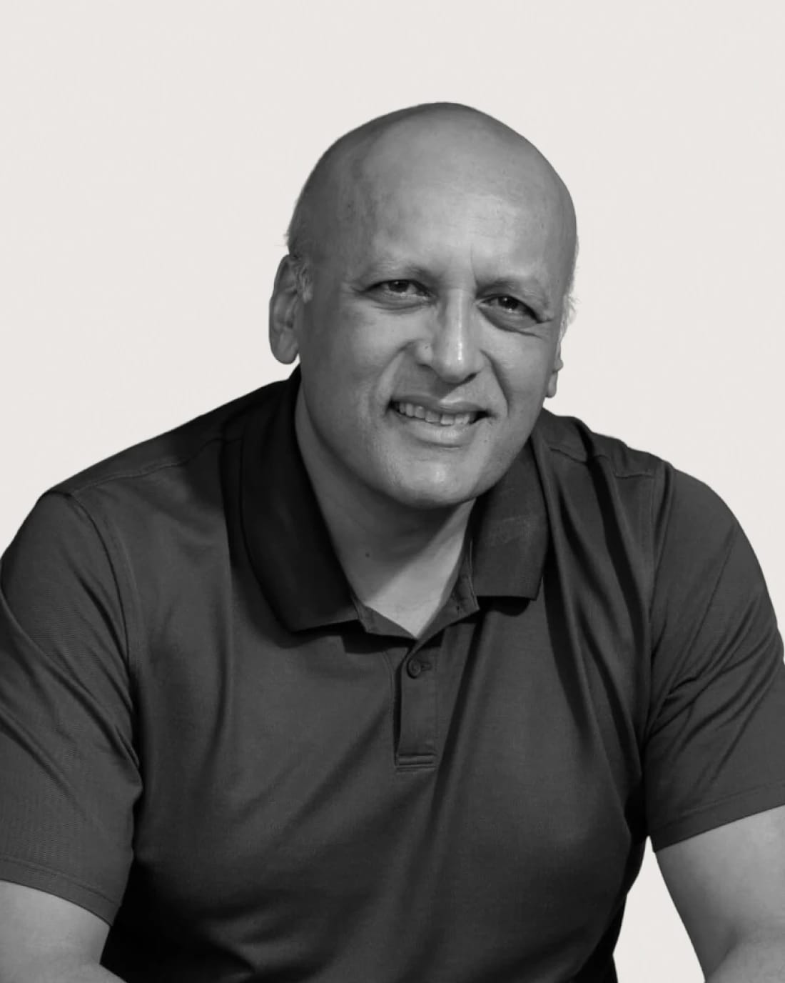 Smiling bald man wearing a navy polo shirt, seated against a light background.