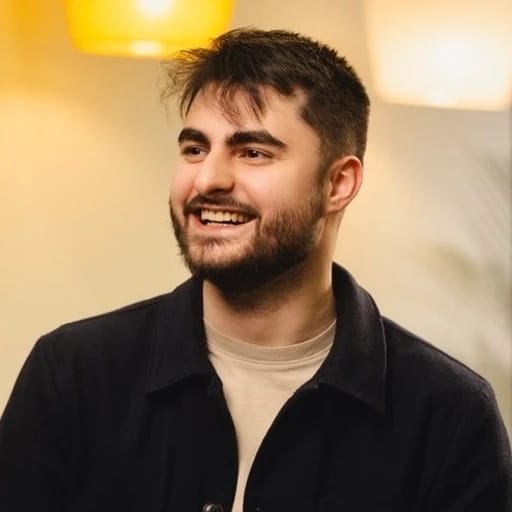 Smiling bearded man in a black jacket and beige shirt.