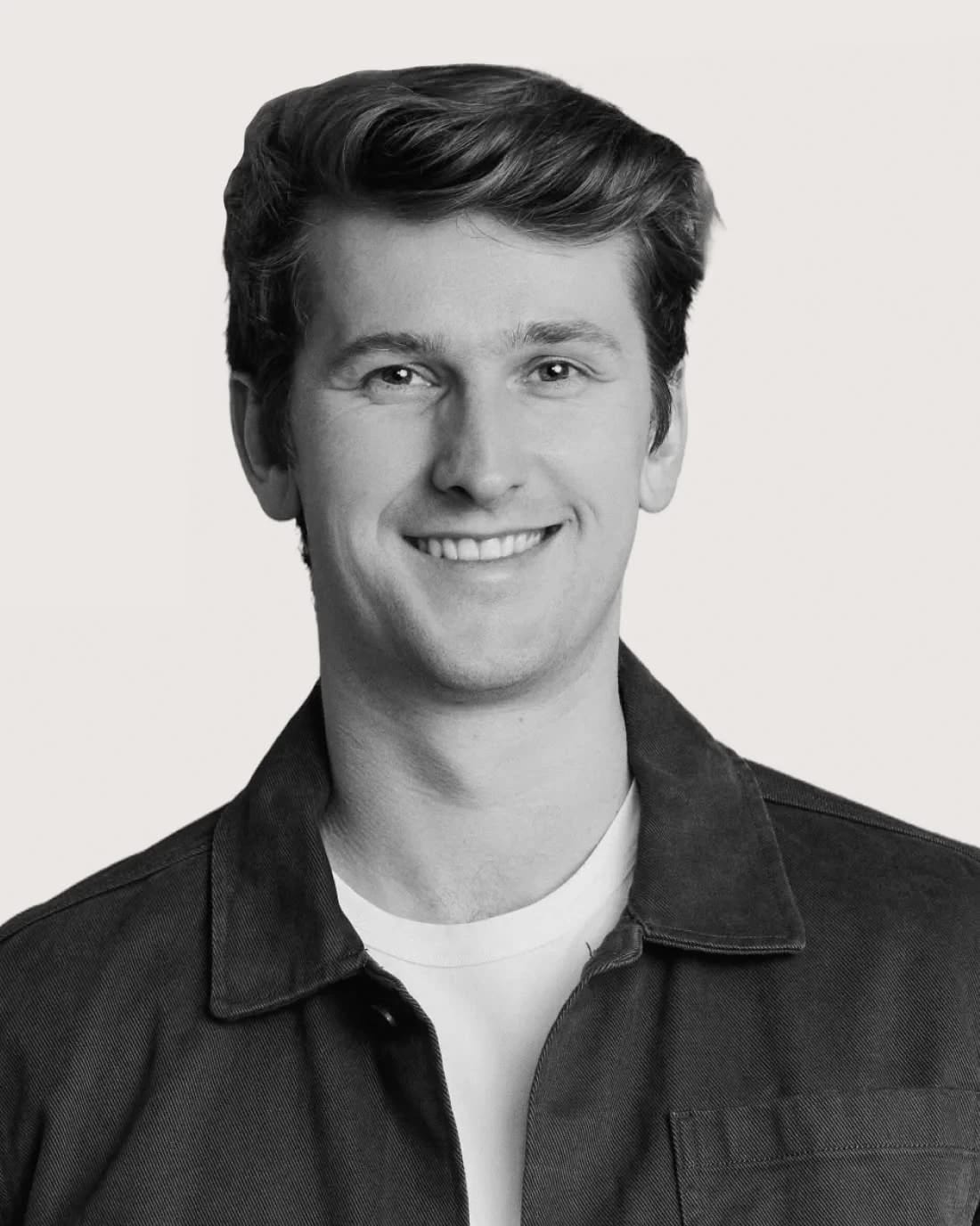 Smiling young man with dark hair wearing a jacket over a white shirt.
