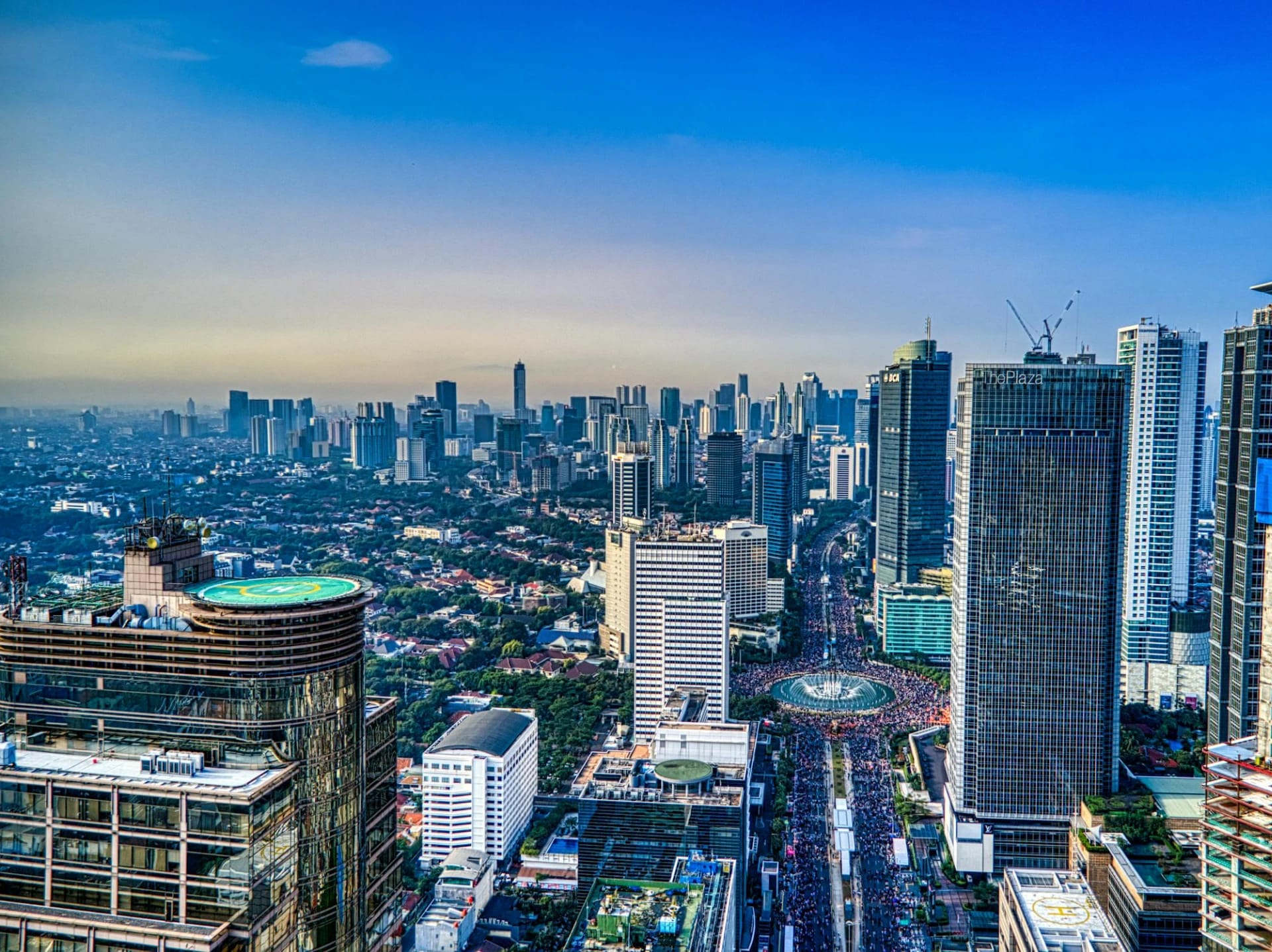 Aerial view of a city skyline with tall skyscrapers, a busy street, and a fountain in the foreground.