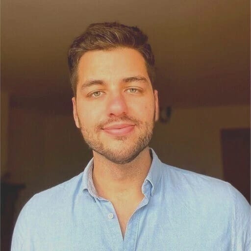 Portrait of a smiling young man with short brown hair and a light blue shirt.